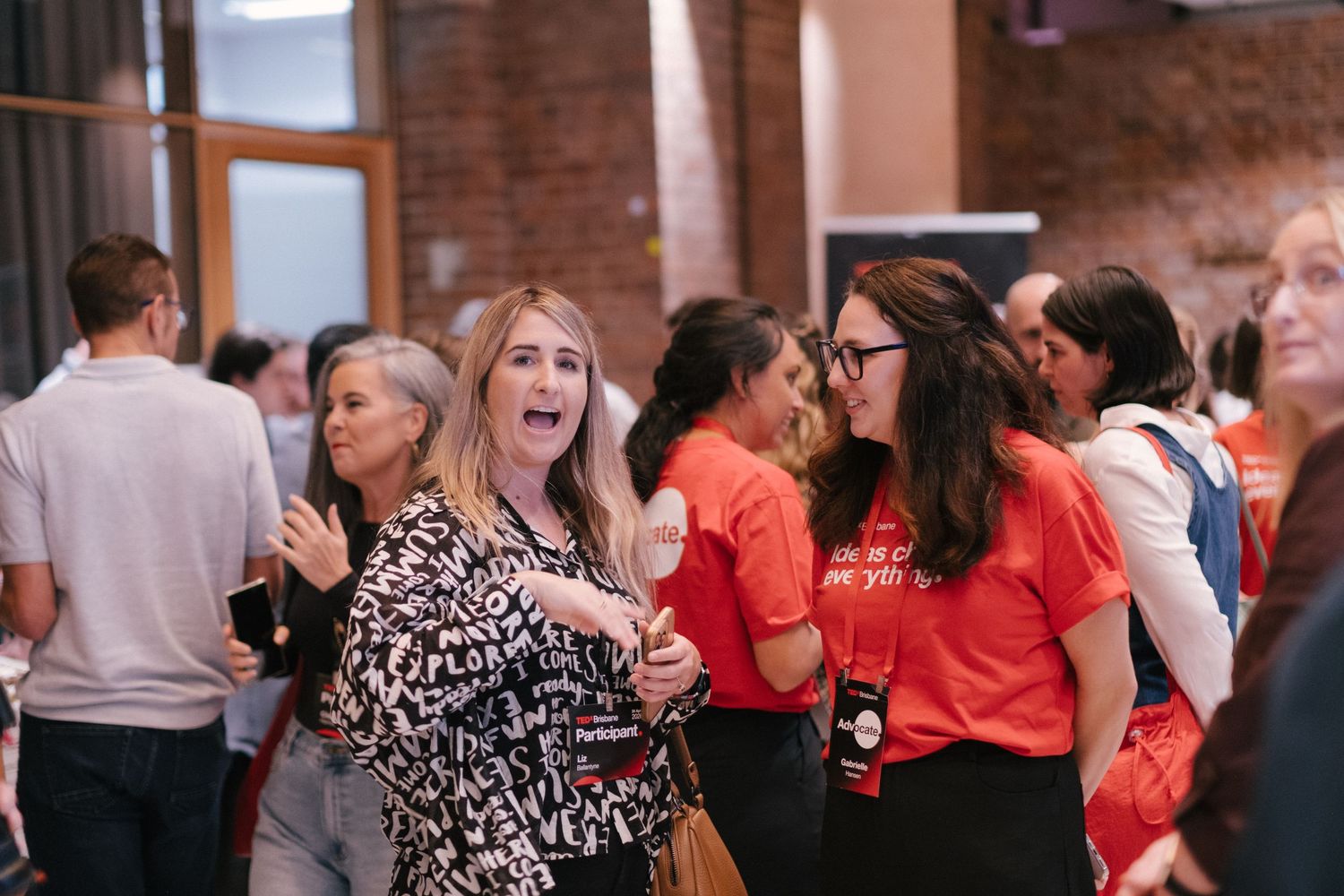 Attendees mingling at TEDx Brisbane event, including volunteers in orange Ideas Change Everything shirts.