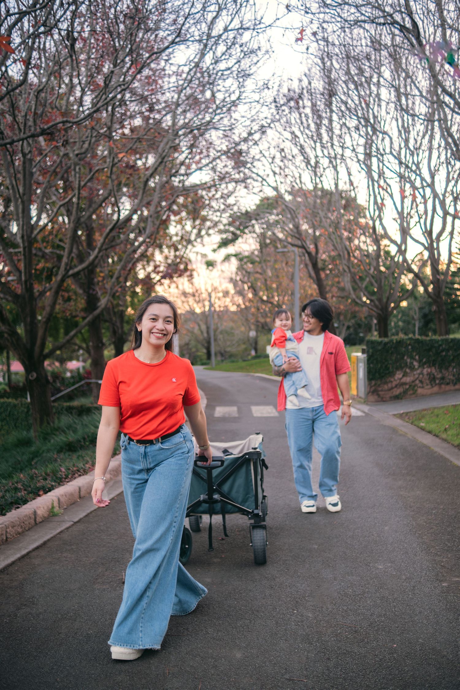 A couple walking outdoors, one pushing a wagon with a toddler.