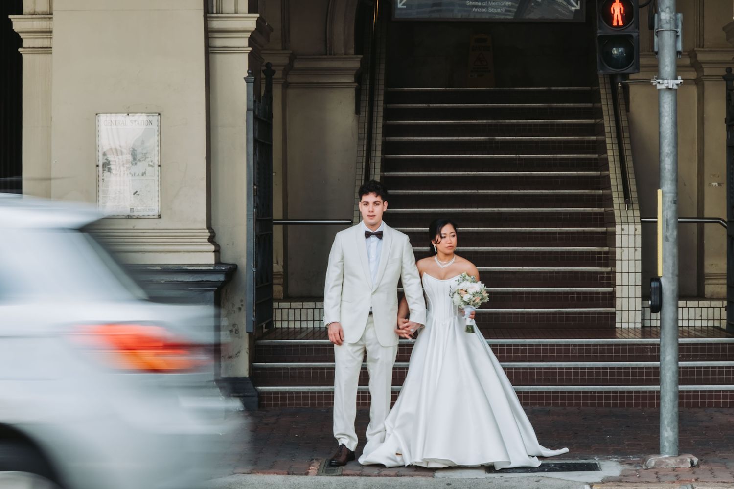 Bride and groom holding hands at urban street corner near historic building staircase on their wedding day.