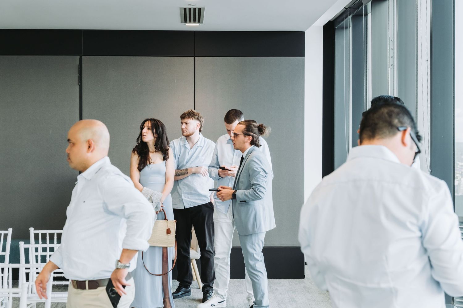 Professionals networking in a modern event space, dressed in smart casual attire, engaged in conversation near large windows.