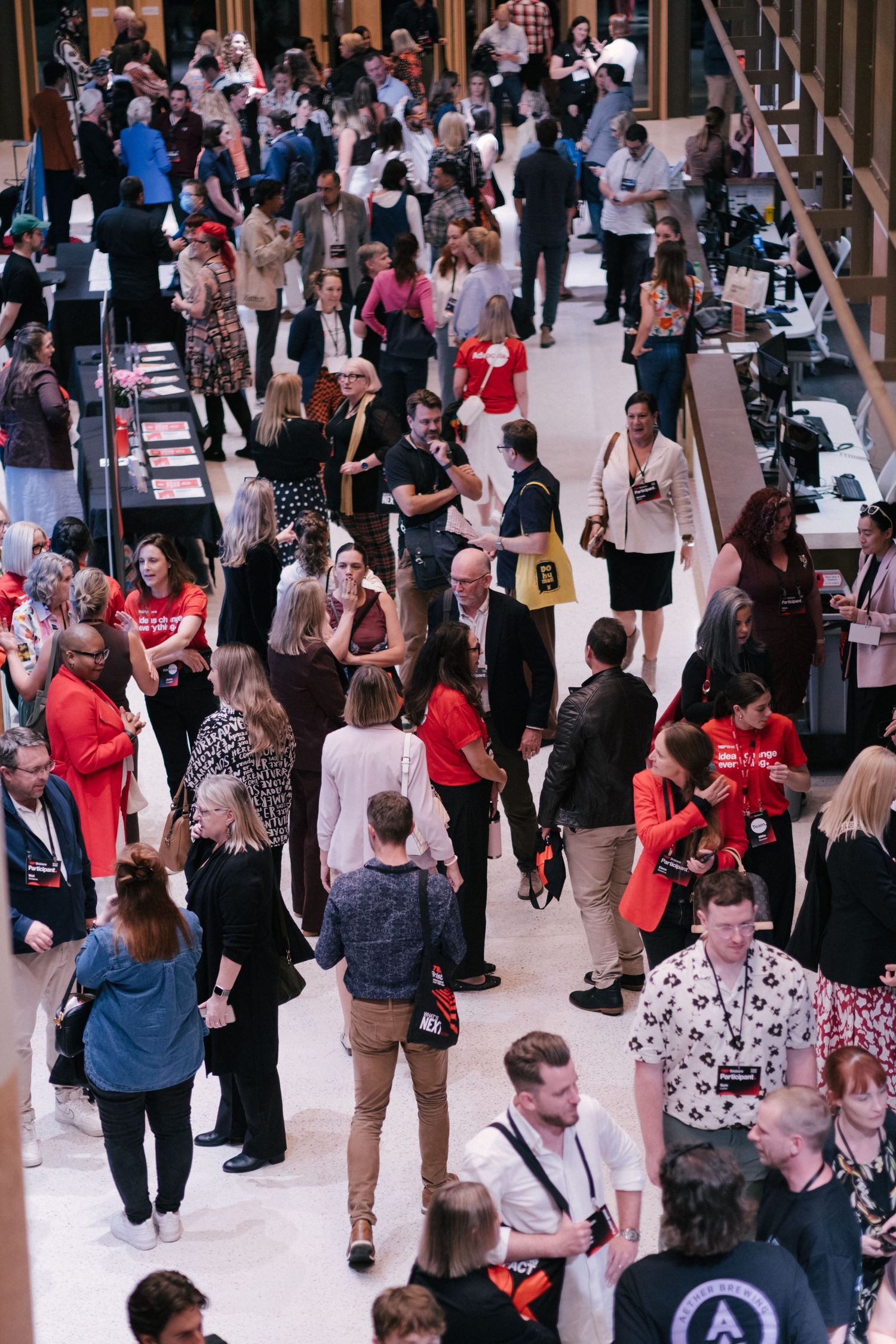 Aerial view of a busy conference hall filled with attendees networking, many wearing lanyards and red accents.