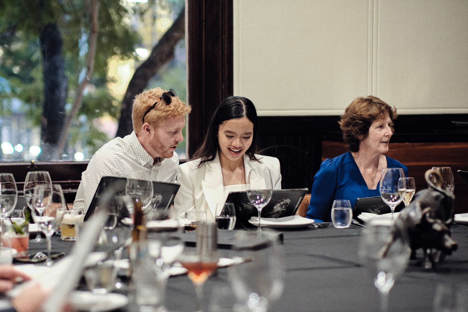 Three people sitting at a table with drinks and food during a wedding reception.
