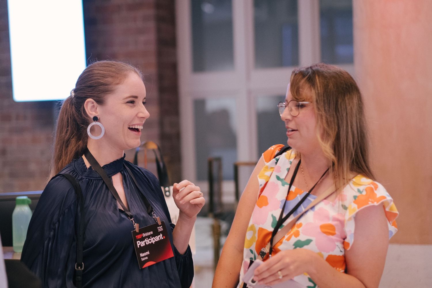 Two women laughing and conversing at TEDx Brisbane networking event wearing participant lanyards.