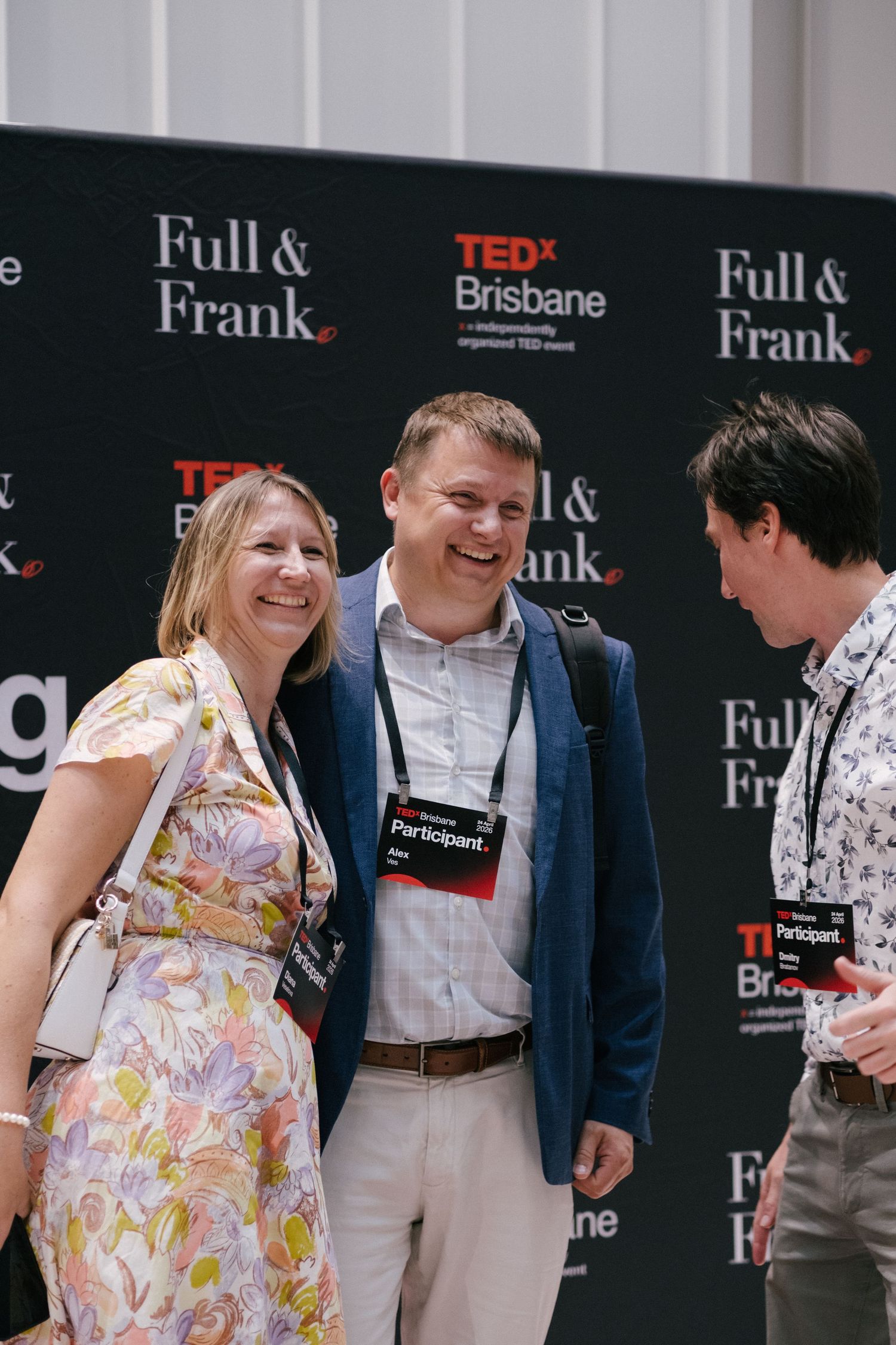 Three smiling TEDx Brisbane participants networking in front of a Full & Frank sponsored backdrop at an event.