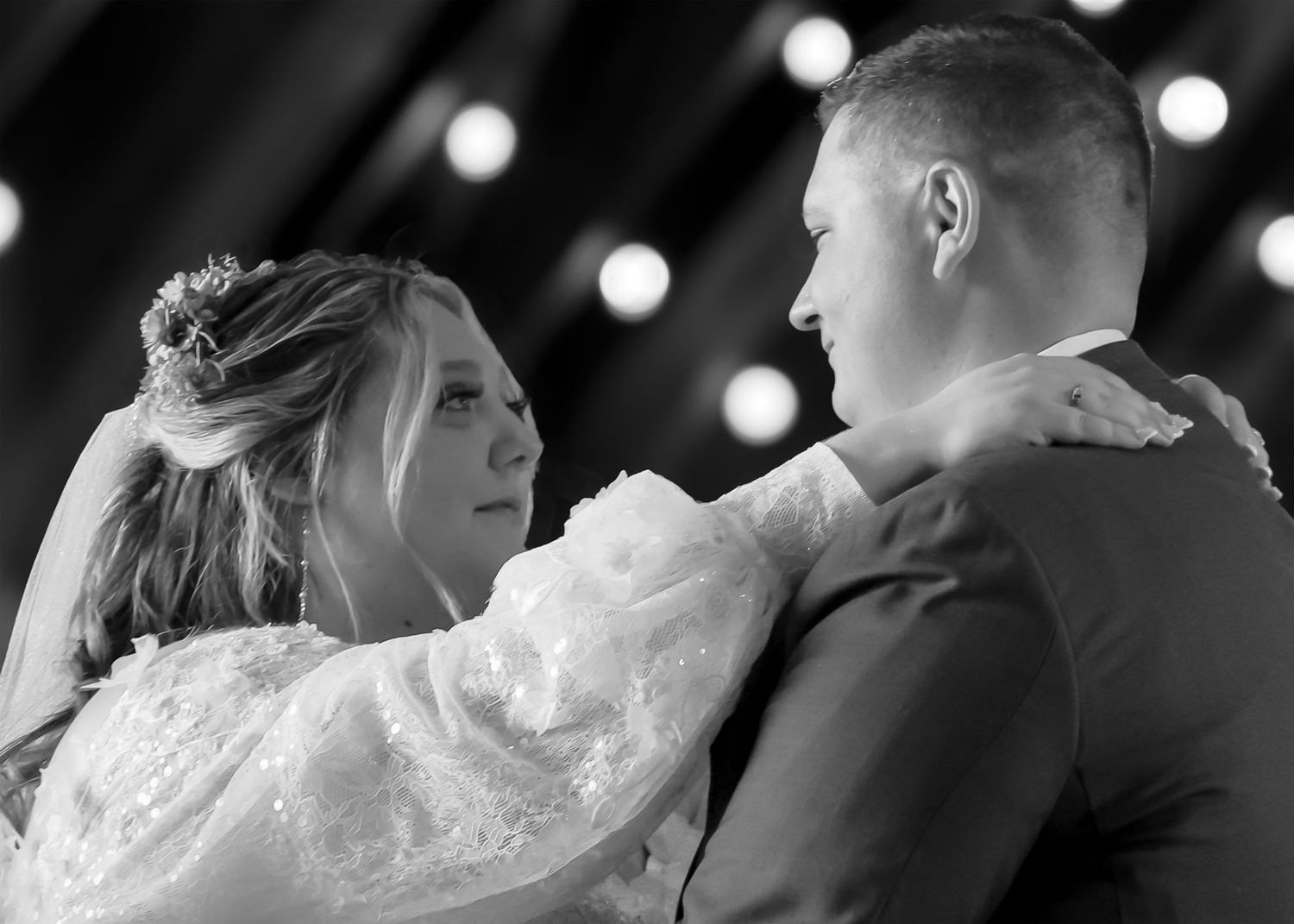 Black and white wedding photo of bride and groom sharing first dance, bride in lace gown with floral hair piece.