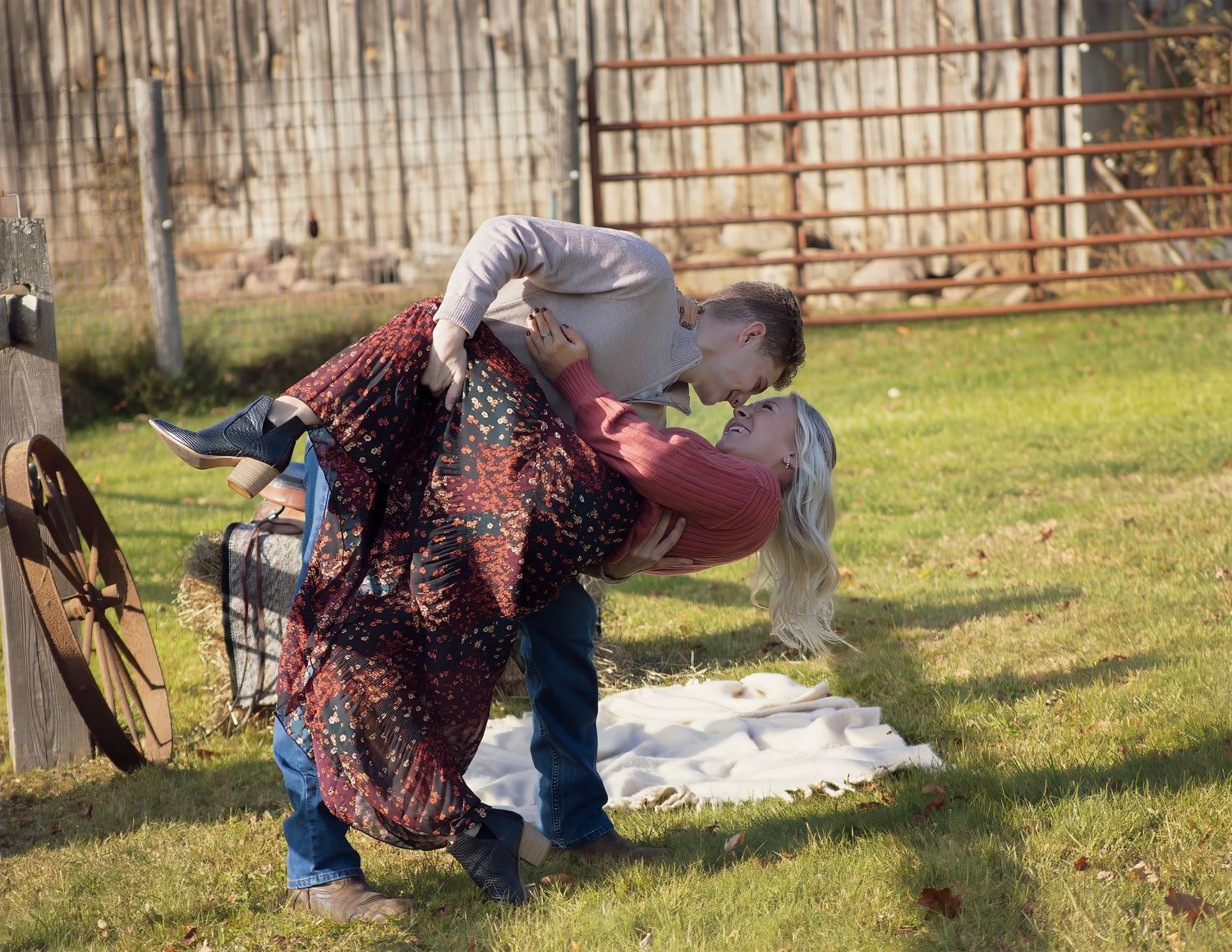 A romantic couple shares a dip kiss in a rustic farm setting on a sunny day.