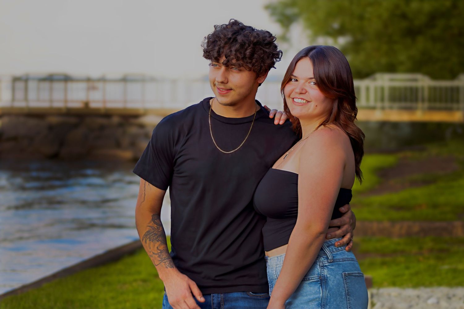 Young couple smiling and embracing outdoors near a waterway on a warm sunny day.