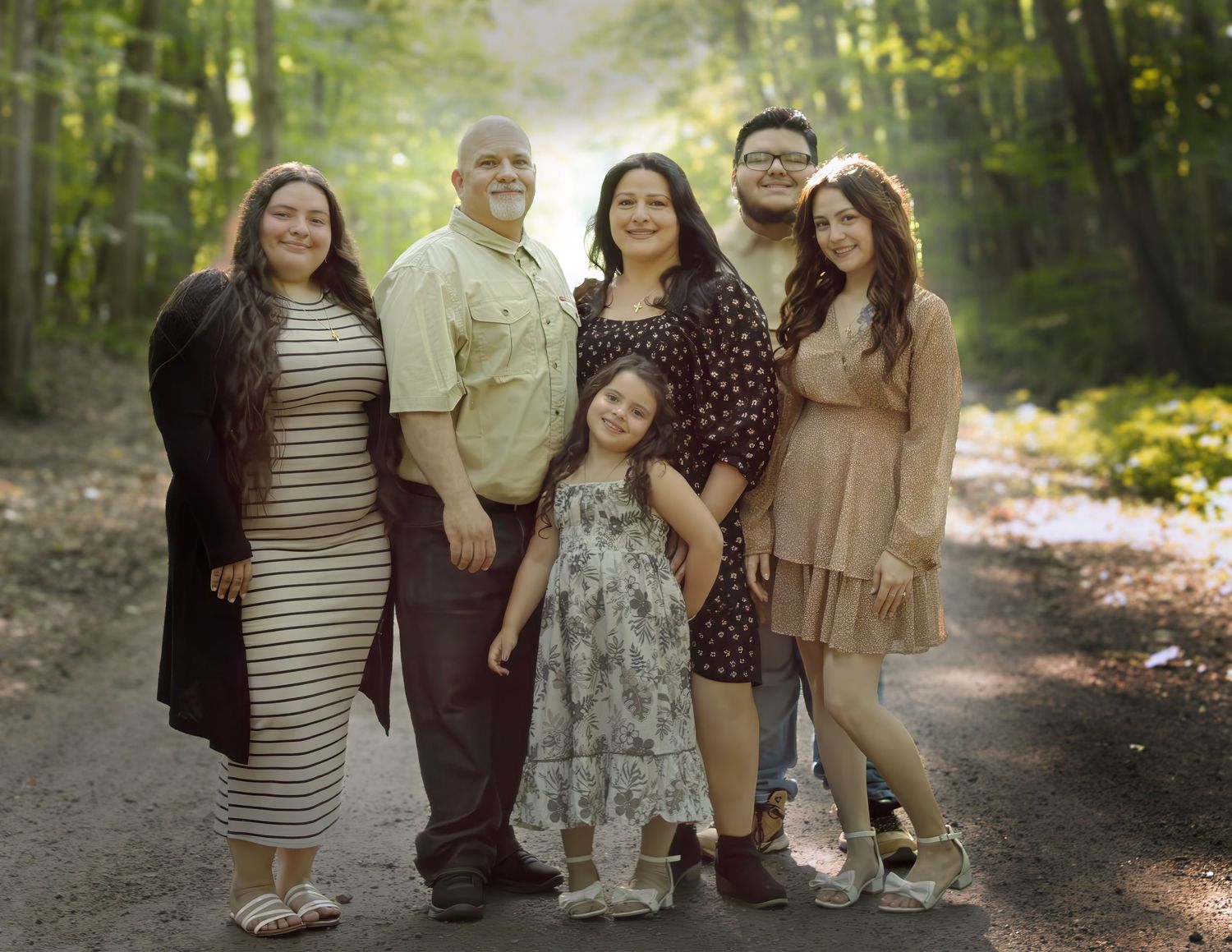 A multigenerational Hispanic family poses together on a forest path surrounded by lush green trees.
