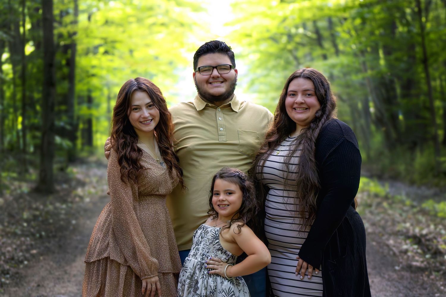 Group of four young adults smiling together on a scenic wooded trail in summer greenery.