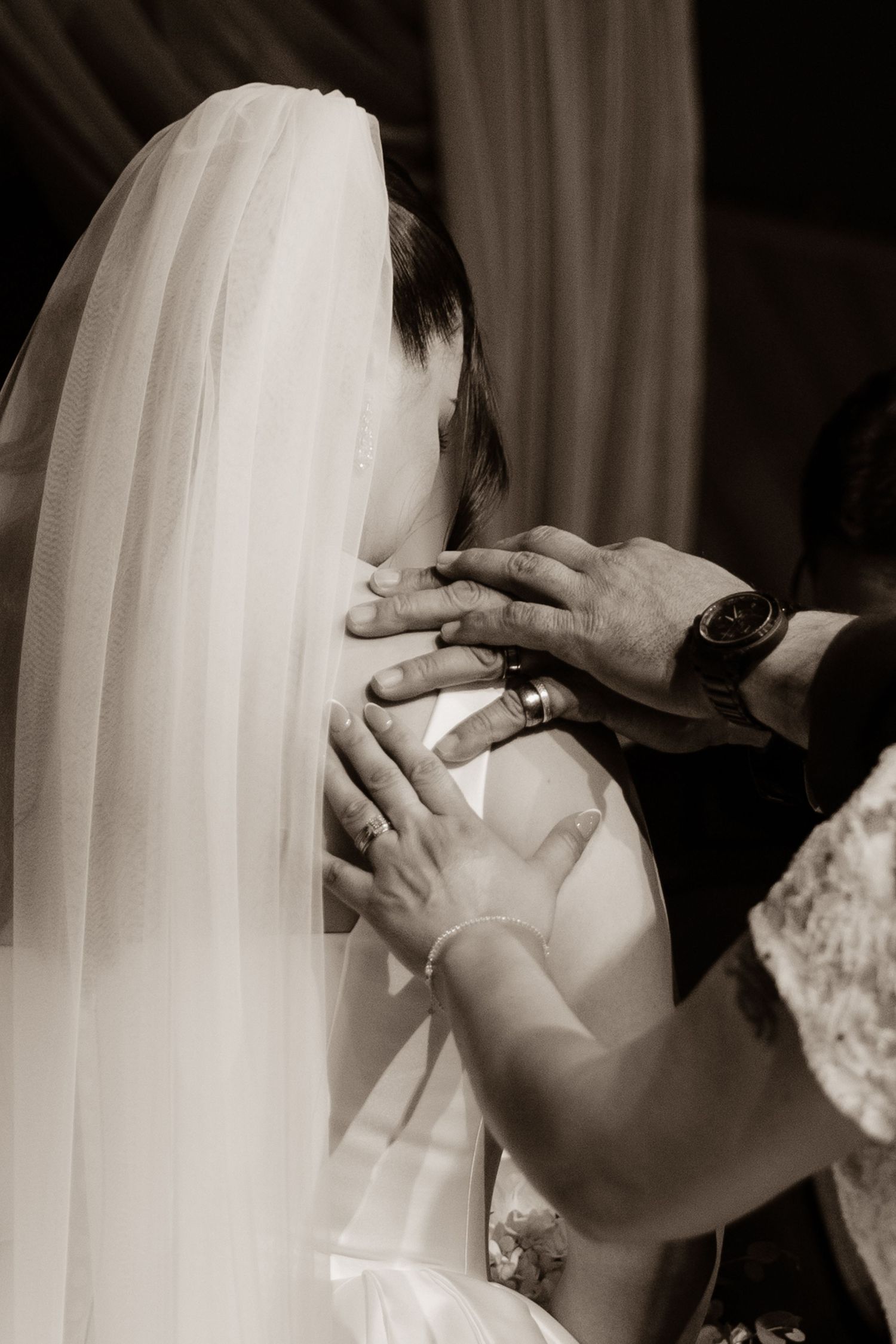 Black and white close-up of hands adjusting a brides veil and dress at a wedding ceremony.