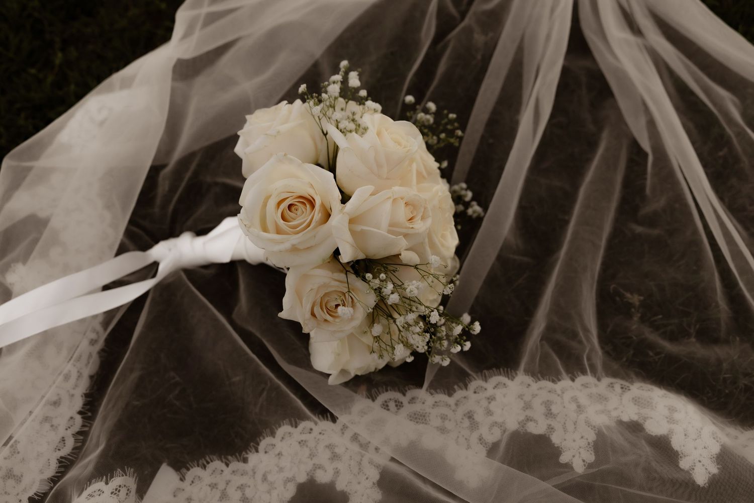 Bridal bouquet of white roses and baby's breath resting on lace wedding veil.