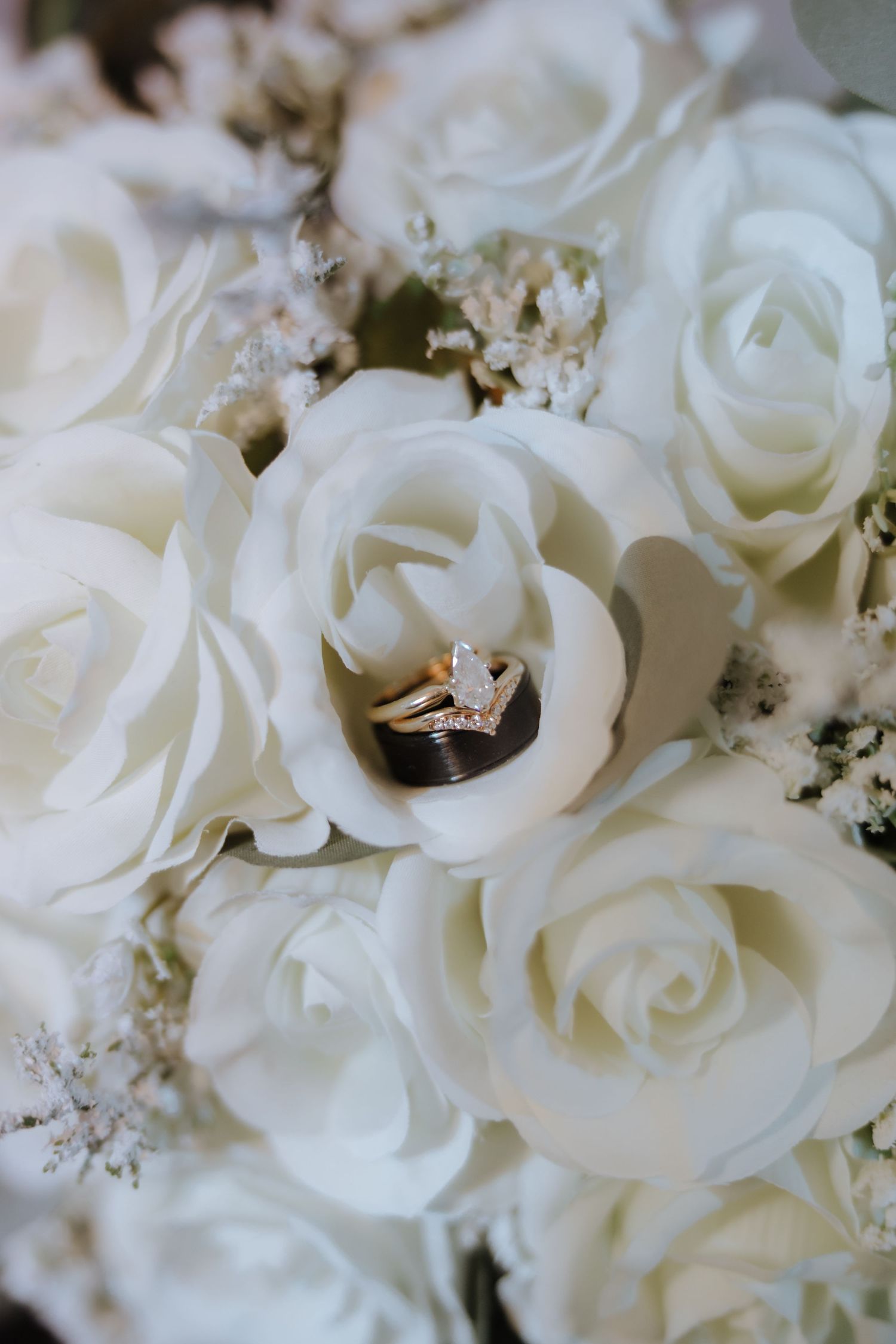 Gold diamond engagement ring and wedding band nestled in white rose bridal bouquet close-up.
