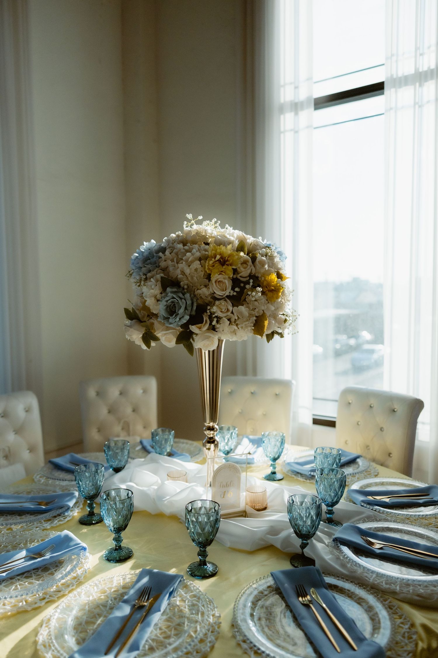 Elegant wedding reception table with blue crystal glasses, gold centerpiece, and floral arrangement.