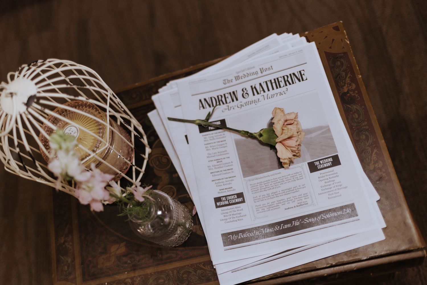 Wedding newspaper programs for Andrew and Katherine displayed on a vintage wooden trunk with floral decor.