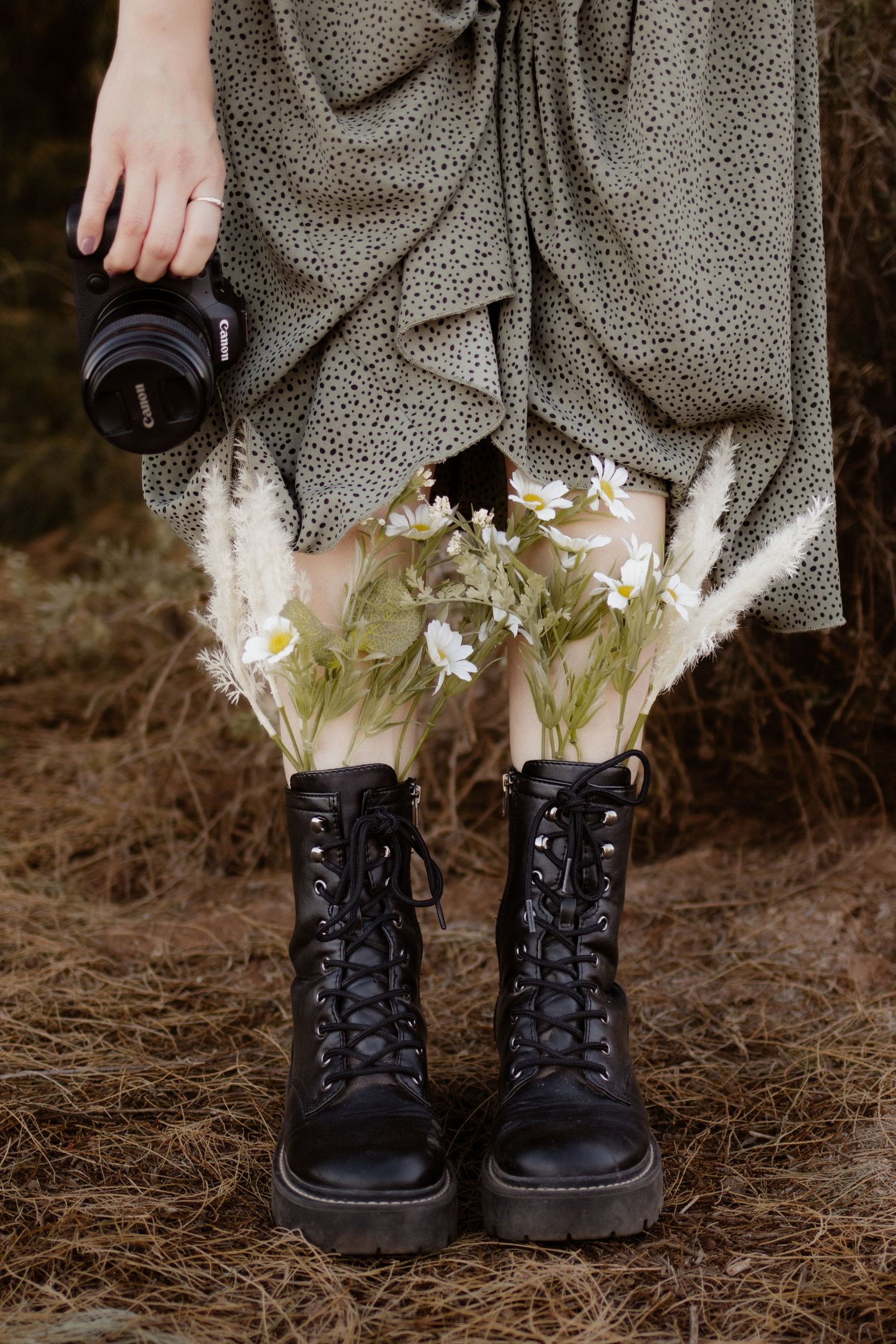Close-up of photographer's boots with wildflowers tucked inside, holding a camera outdoors.