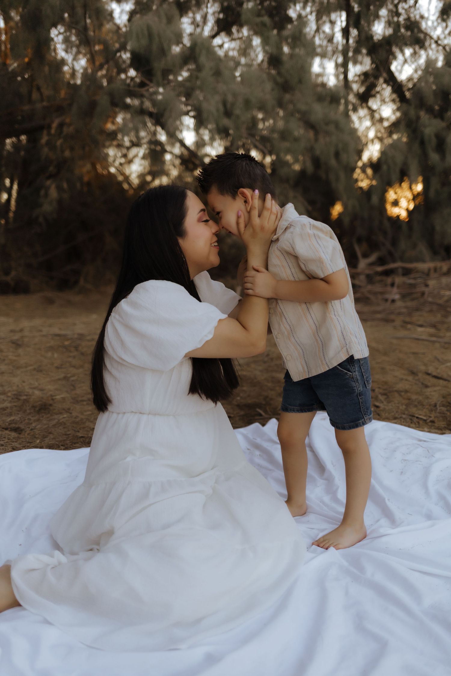 Mother and young child sharing a tender forehead touch on white blanket outdoors.