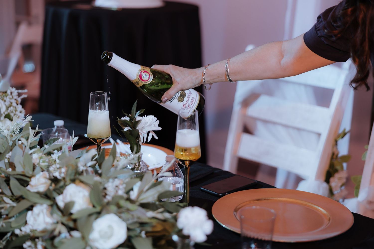 Champagne being poured into glasses at wedding head table decorated with white flowers and copper chargers.