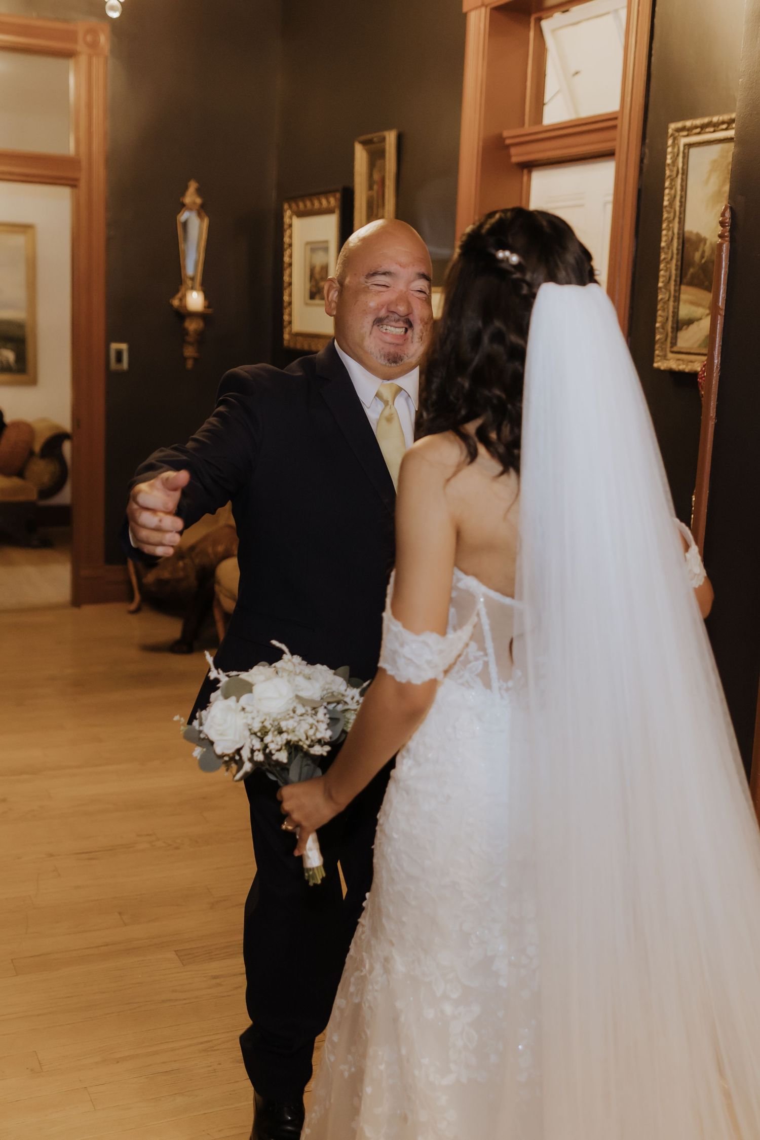 Emotional father reacting with joy upon seeing his daughter in her lace wedding gown and veil.