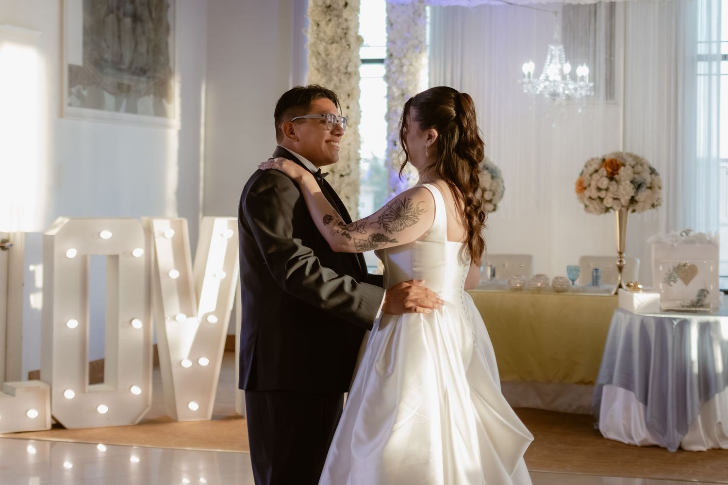 Bride and groom share their first dance in a decorated ballroom with illuminated LOVE letters in the background.