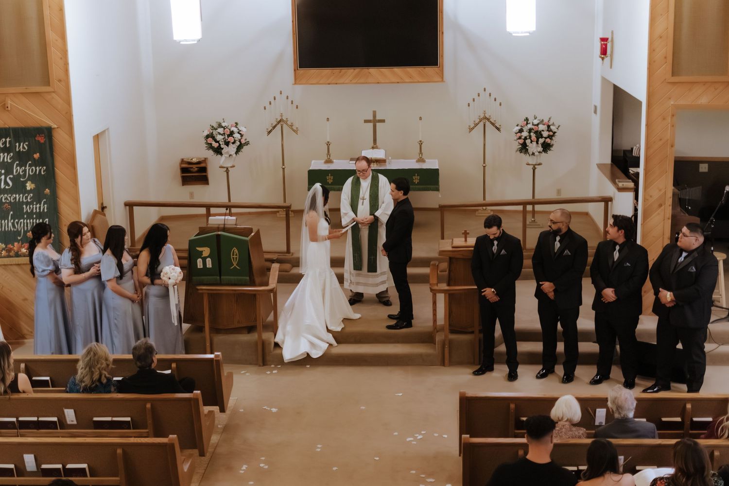 Wedding ceremony in a rustic church with bridesmaids, groomsmen, and officiant at the altar.