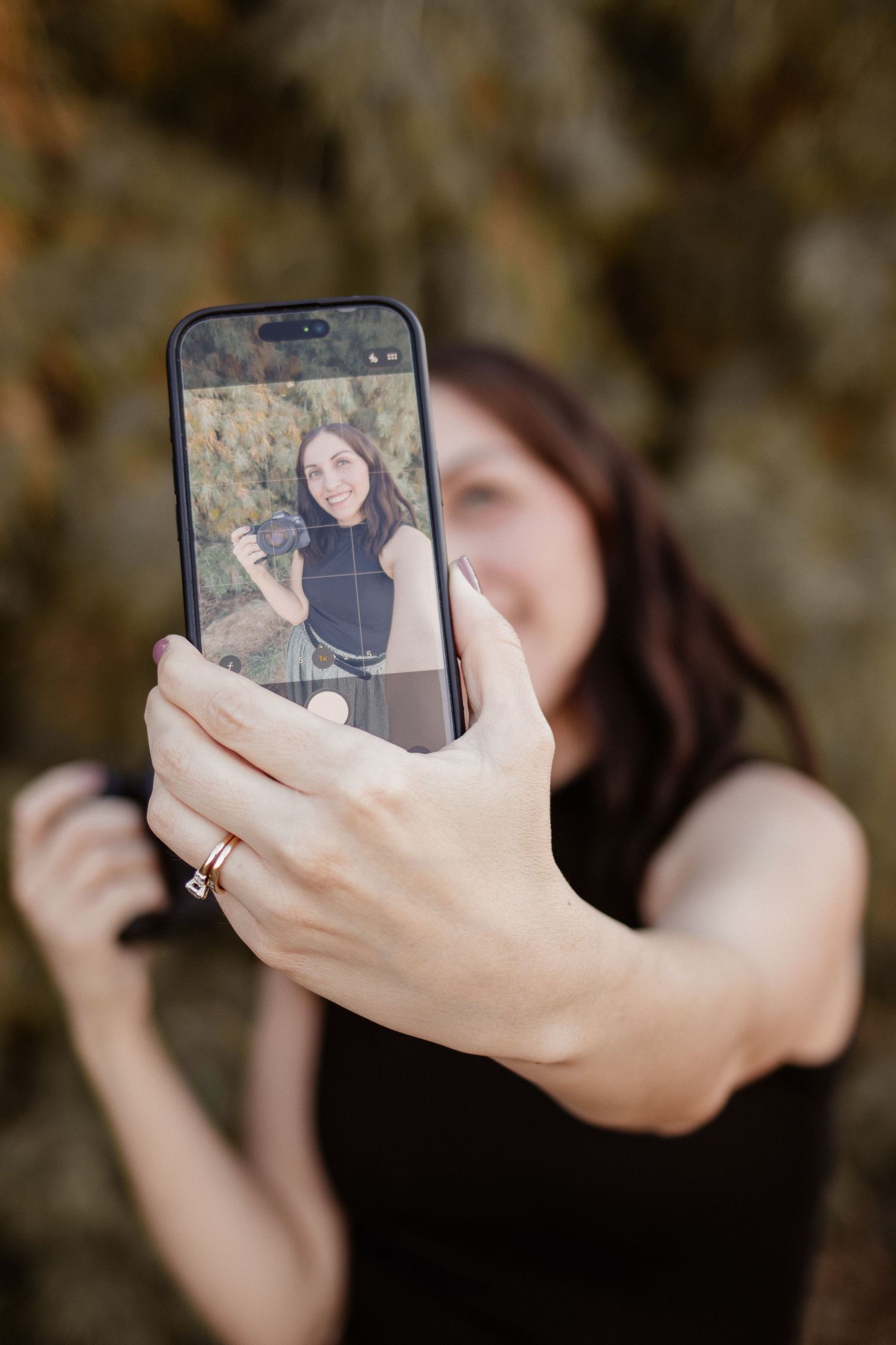 Female photographer taking a selfie with phone, showing image on screen outdoors.