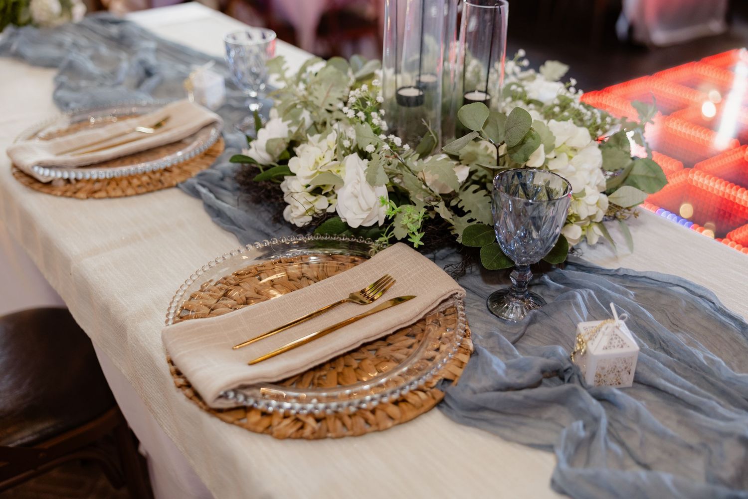 Elegant wedding reception table with wicker charger plates, linen napkins, and white floral centerpiece.