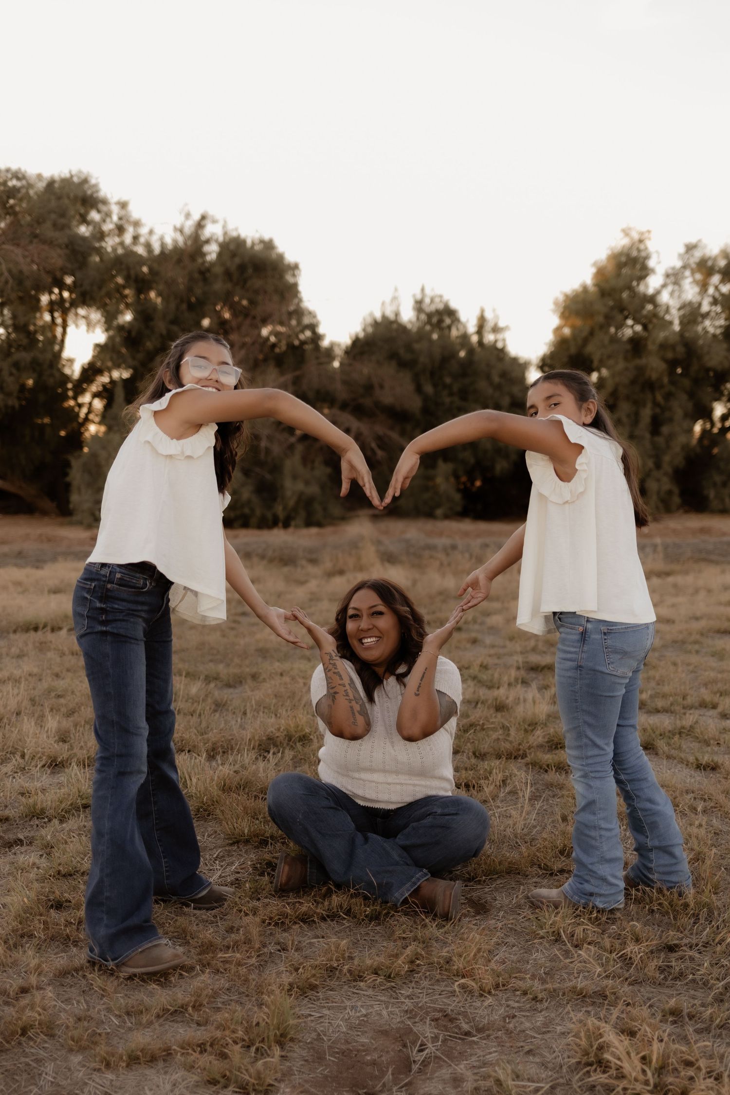Mother and two daughters forming a heart shape with their arms in an open field.