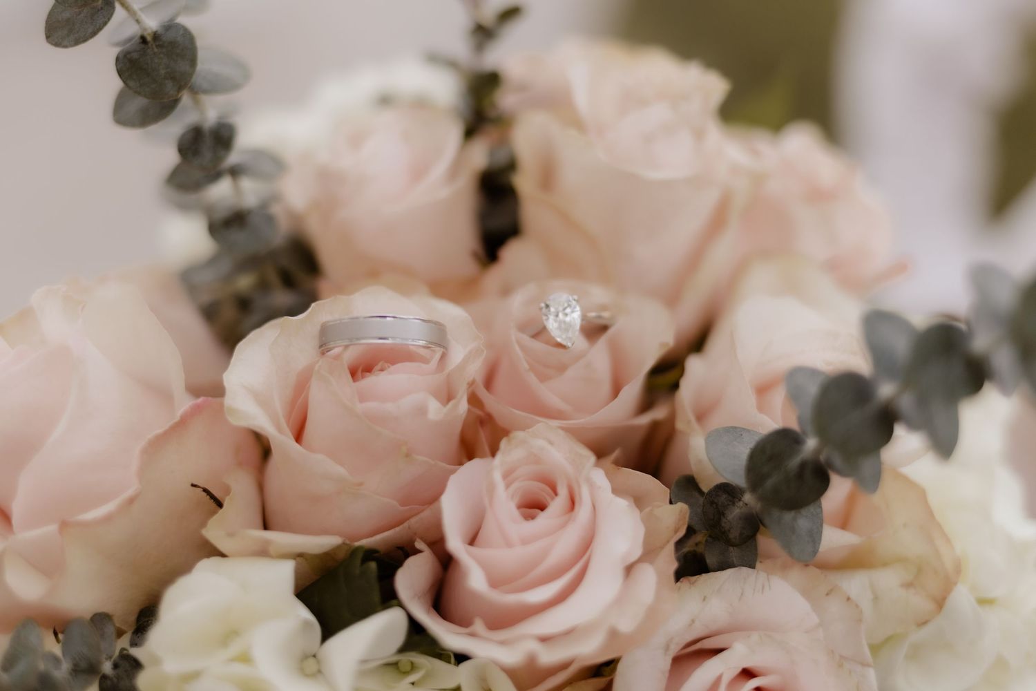 Elegant wedding rings resting on blush pink roses in a bridal bouquet with eucalyptus greenery.