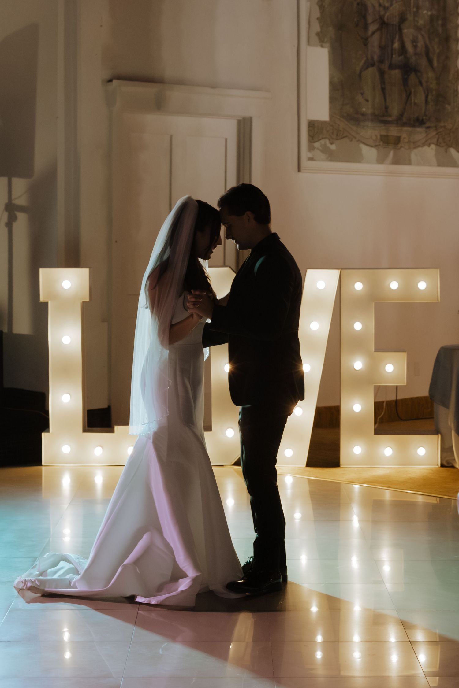 Bride and groom sharing first dance silhouetted against large illuminated LOVE marquee letters.