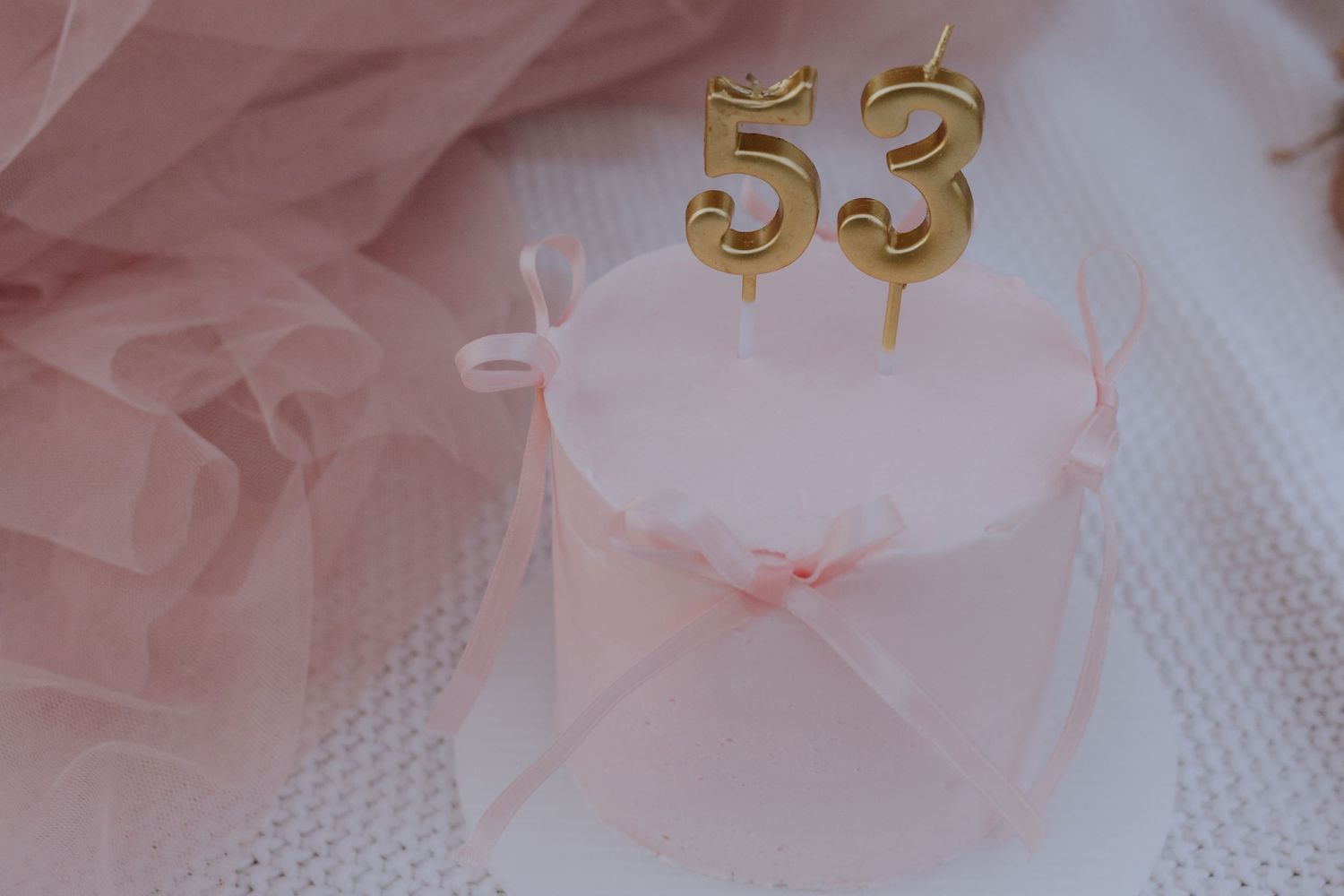 Gold number 53 birthday candles on a small pink cake wrapped in pink tulle.