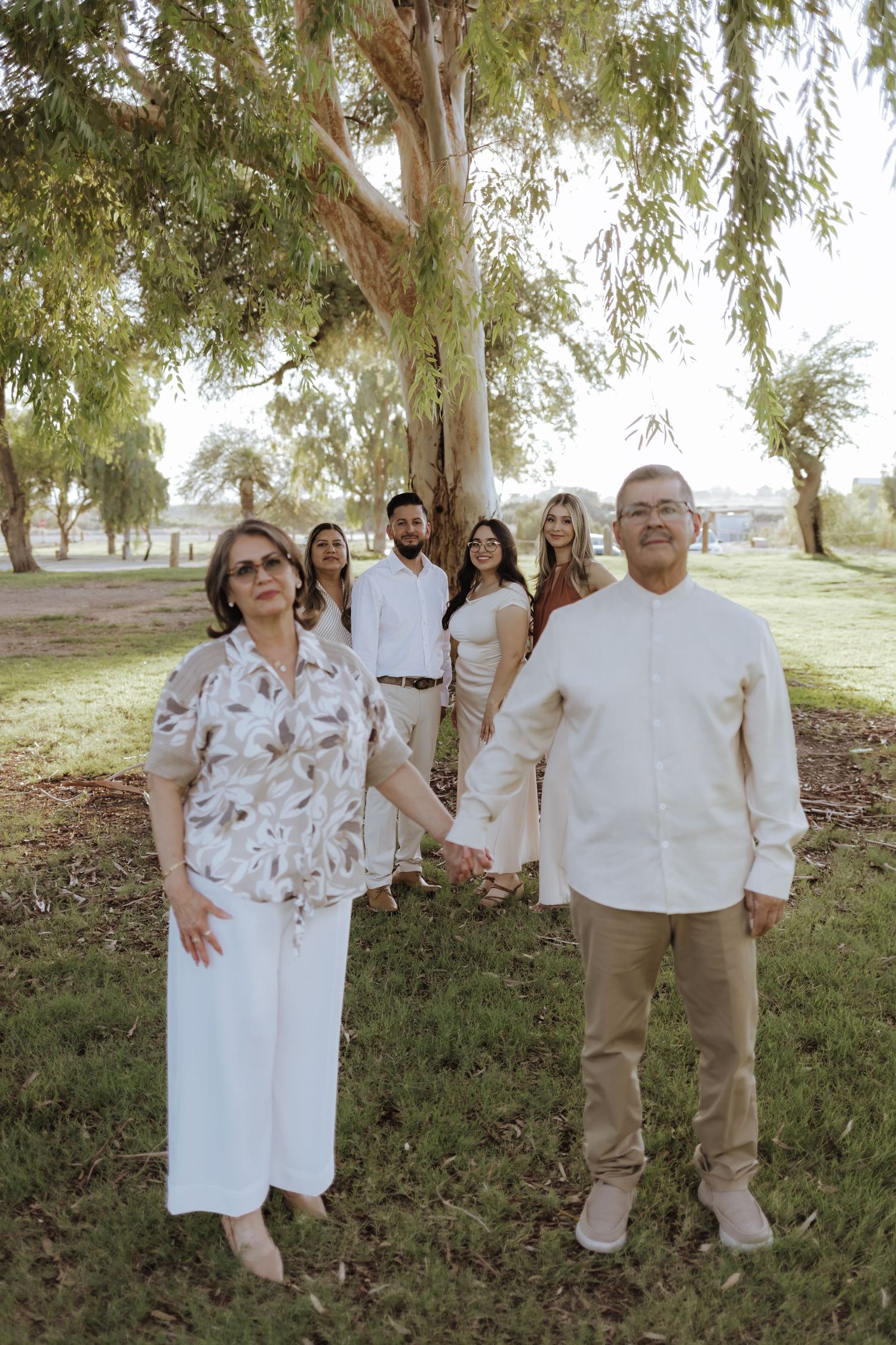 Older couple holds hands in park with family members standing behind them outdoors.