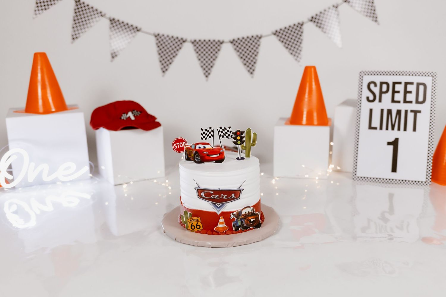 Cars-themed first birthday smash cake with Lightning McQueen decorations, orange traffic cones, and a Speed Limit 1 sign.