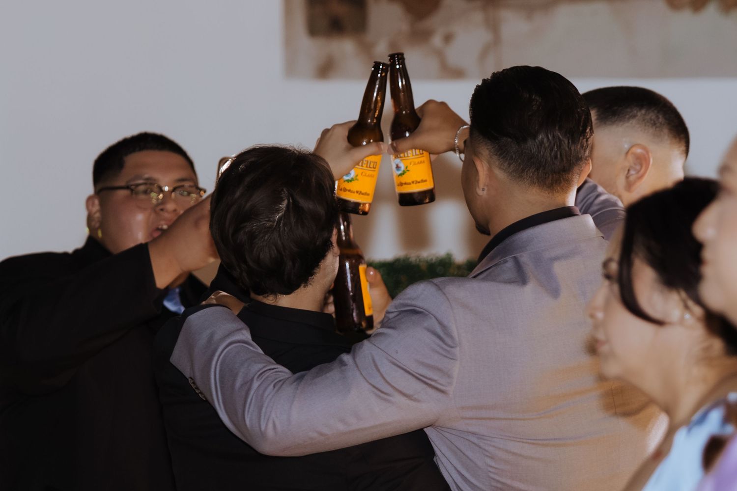 Group of men clinking beer bottles together in a celebratory toast at a wedding reception.