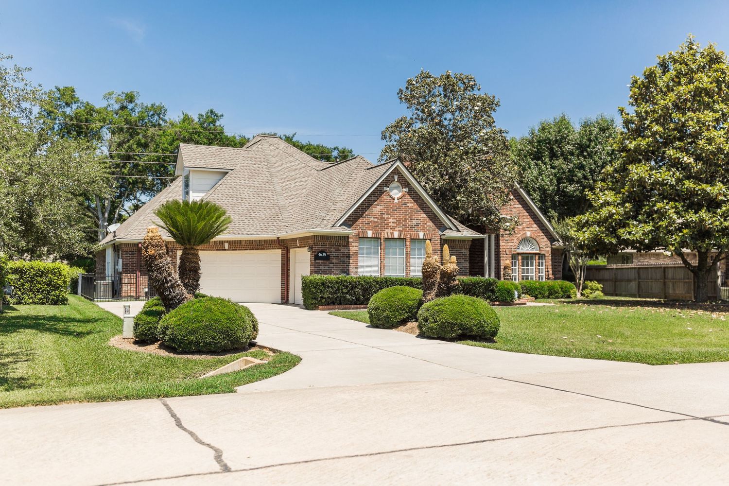 Brick ranch home with manicured lawn, mature trees, and wide concrete driveway.