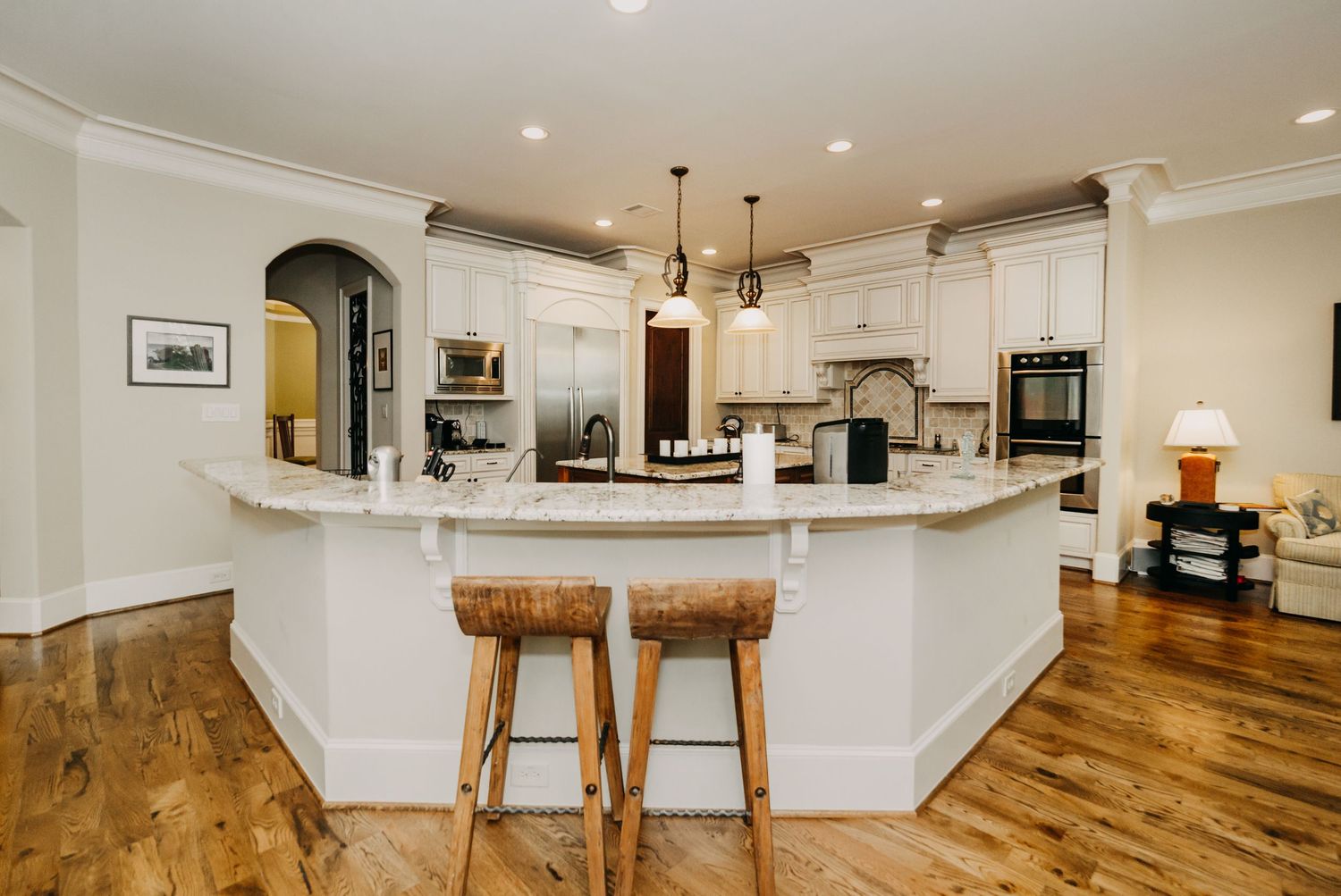 Elegant kitchen with white cabinets, curved island, marble countertops, and two wooden bar stools.