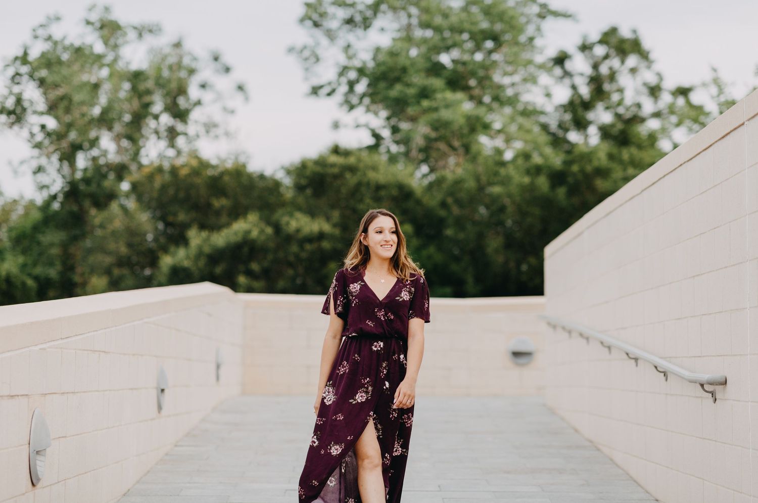 Woman in floral burgundy maxi dress walking down outdoor steps with lush green trees in background.