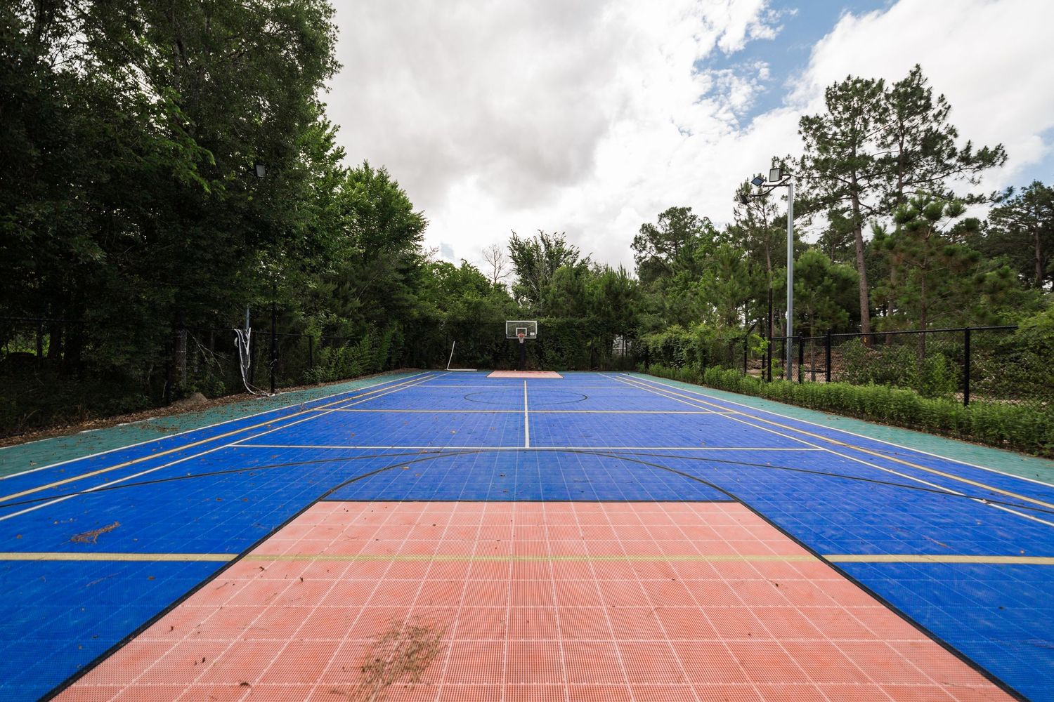 Full-size outdoor sports court with blue and red surface and basketball hoop.