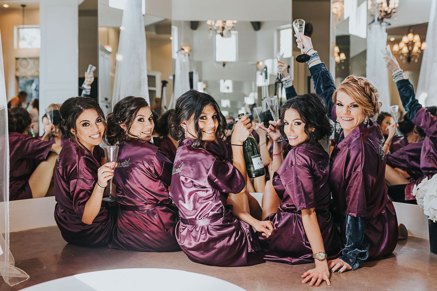 Bridesmaids in purple satin robes celebrating together on the floor with champagne.