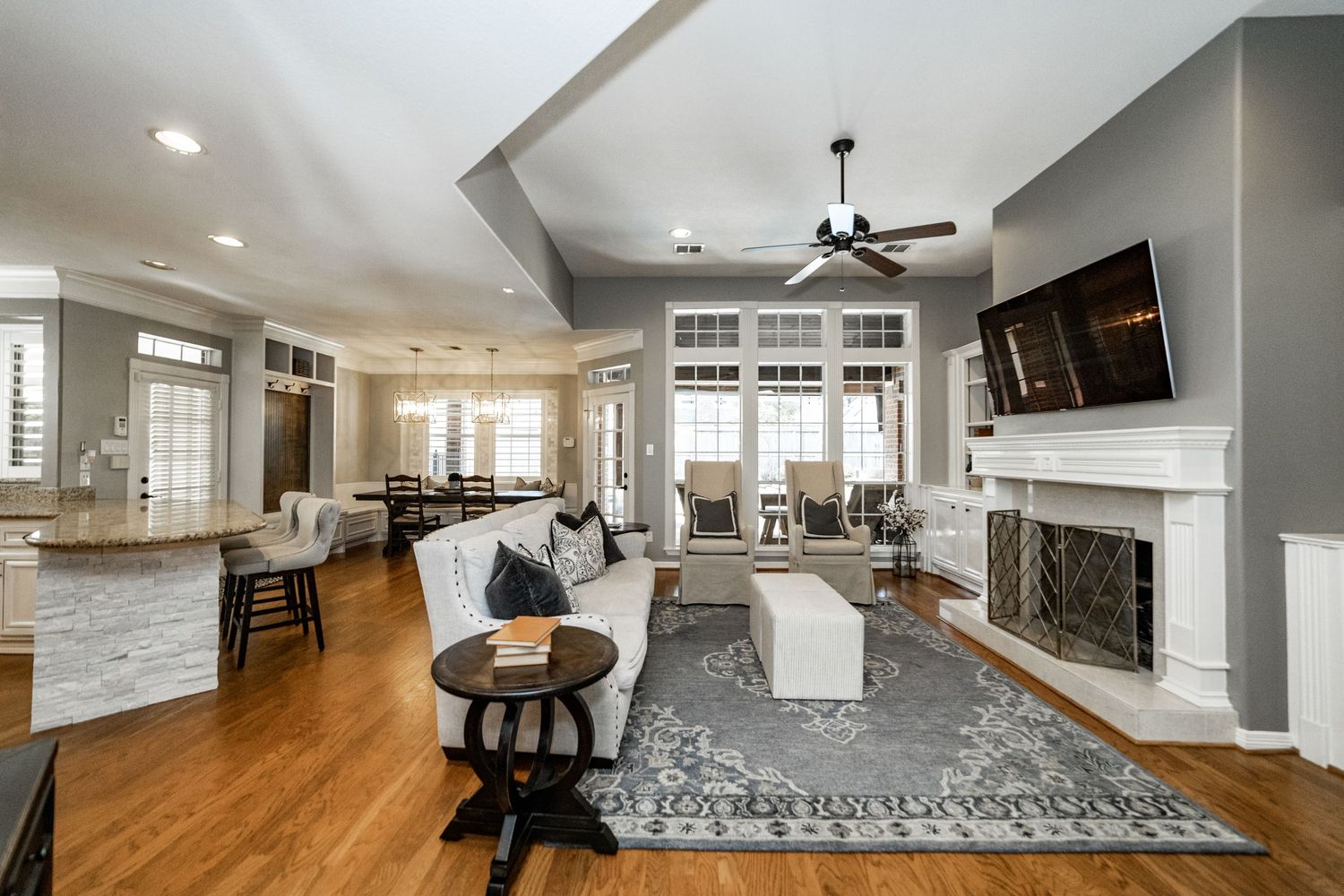 Spacious open-concept living room with hardwood floors, fireplace, ceiling fan, and modern decor connecting to kitchen.