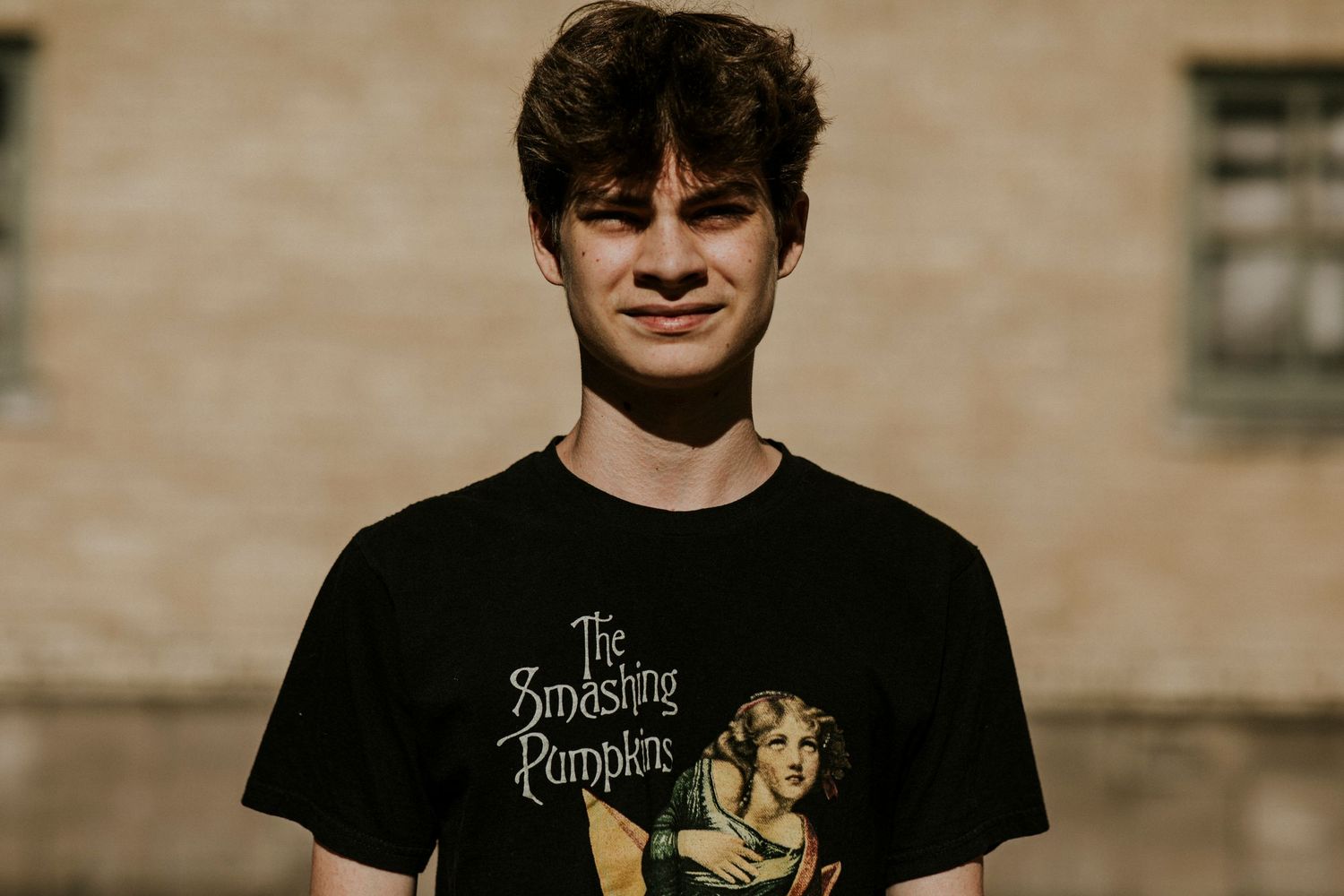 Young man wearing a black Smashing Pumpkins band t-shirt standing outdoors against a stone building.