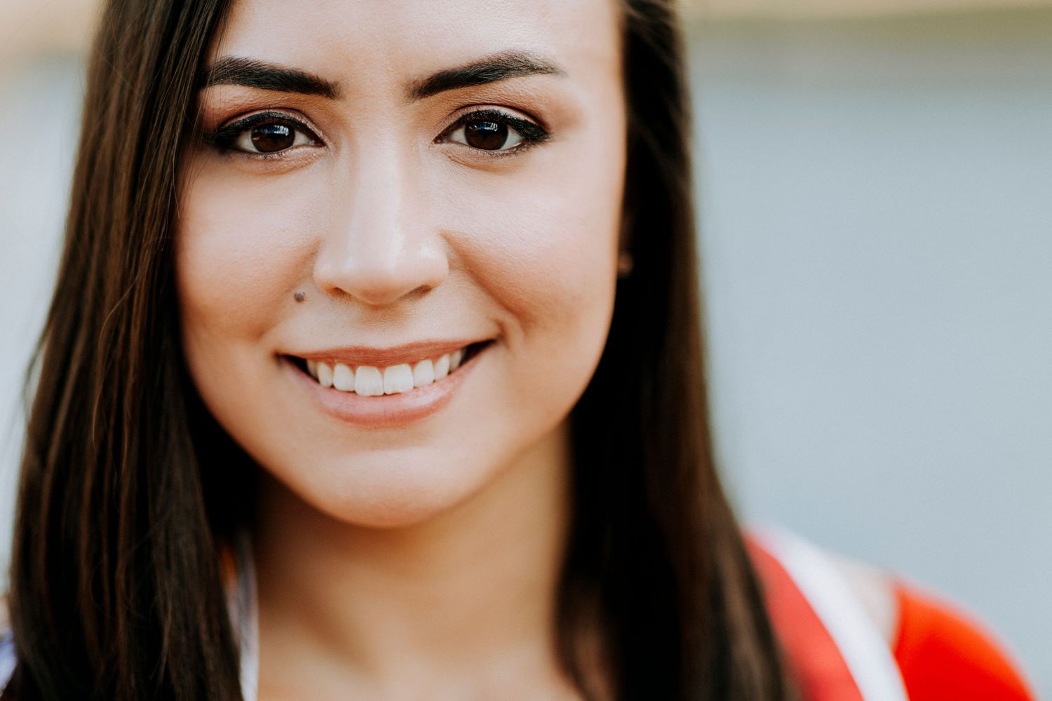 Smiling young woman with long dark hair wearing a red top, close-up portrait photo.