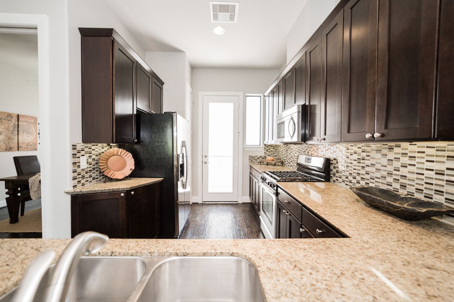Modern kitchen with dark wood cabinets, granite countertops, stainless steel appliances, and mosaic tile backsplash.