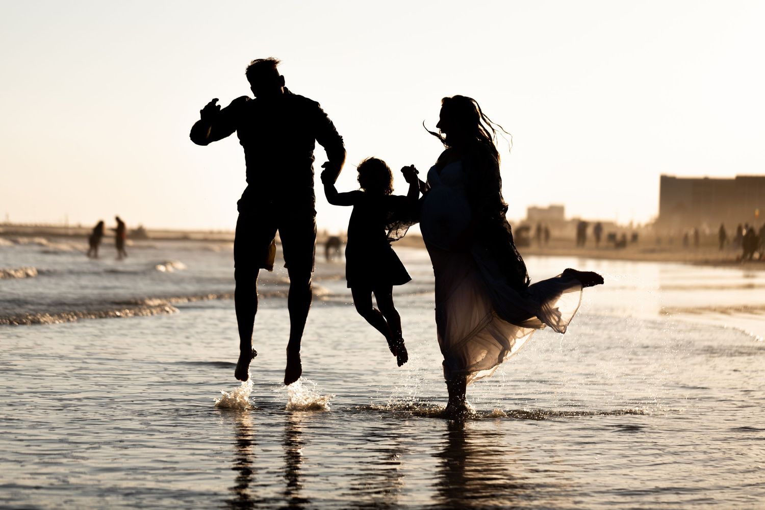 Family silhouette jumping joyfully on a sunny beach at sunset.