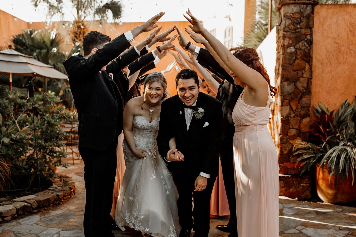 Smiling newlyweds walking through an arch of raised hands at outdoor wedding.