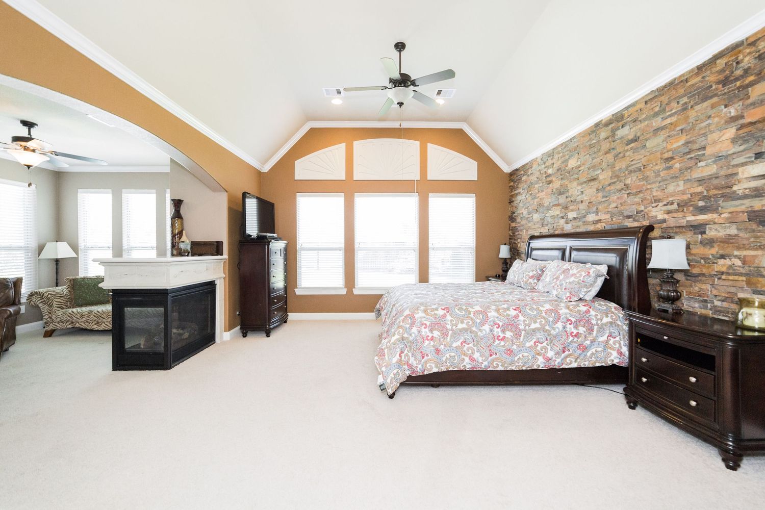 Spacious master bedroom with vaulted ceiling, stone accent wall, fireplace, and large wooden bed frame.