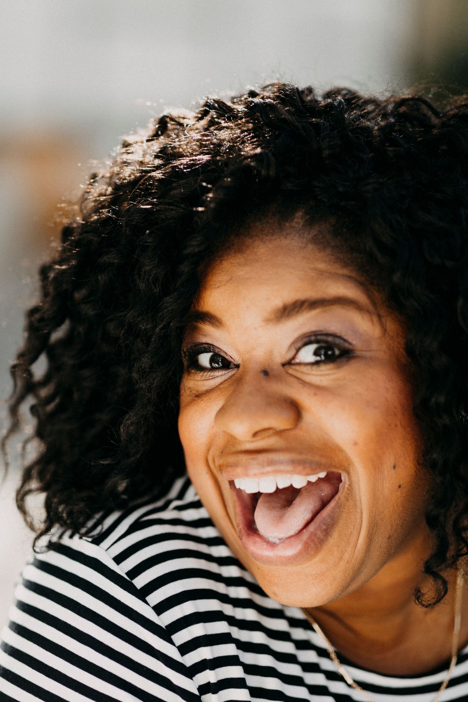 Close-up of a laughing Black woman with curly hair wearing a striped shirt.