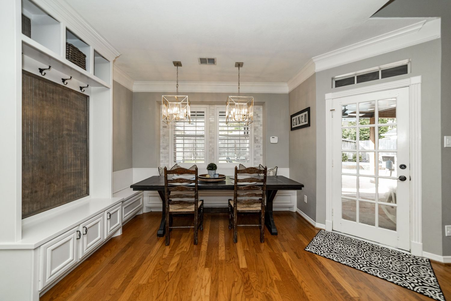 Elegant dining room with hardwood floors, wainscoting, pendant lights, dark wood table, and French door leading to patio.