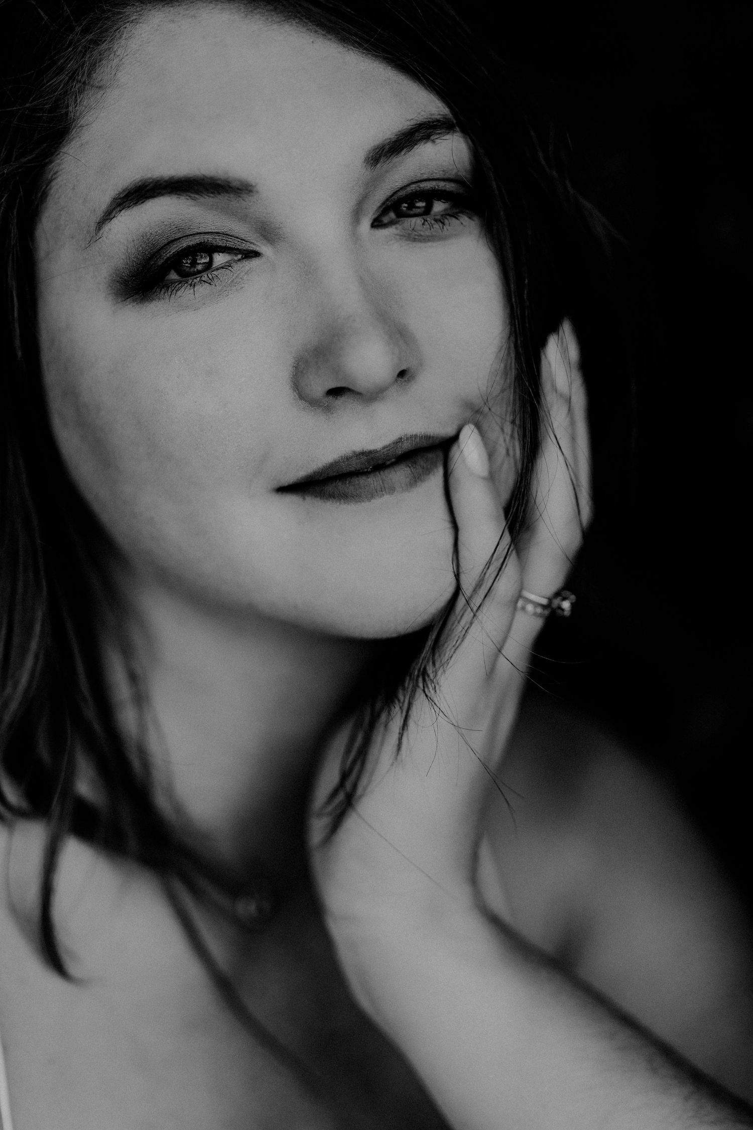 Black and white portrait of a young woman with dark hair resting her hand on her cheek, wearing a ring.