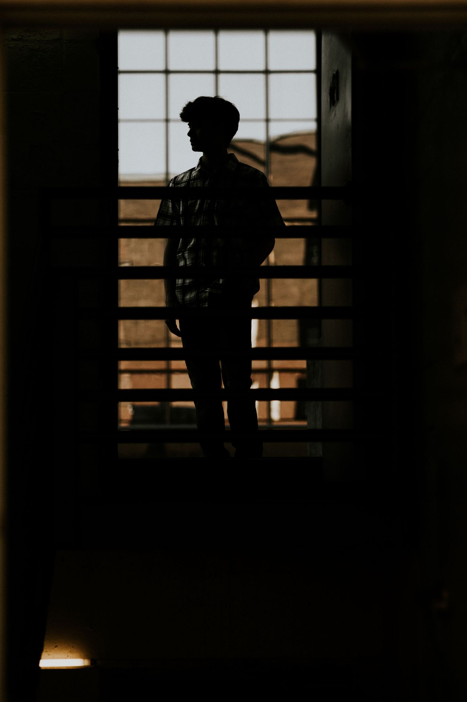 Silhouette of a young man standing in front of a large window with golden light, creating a dramatic dark contrast.