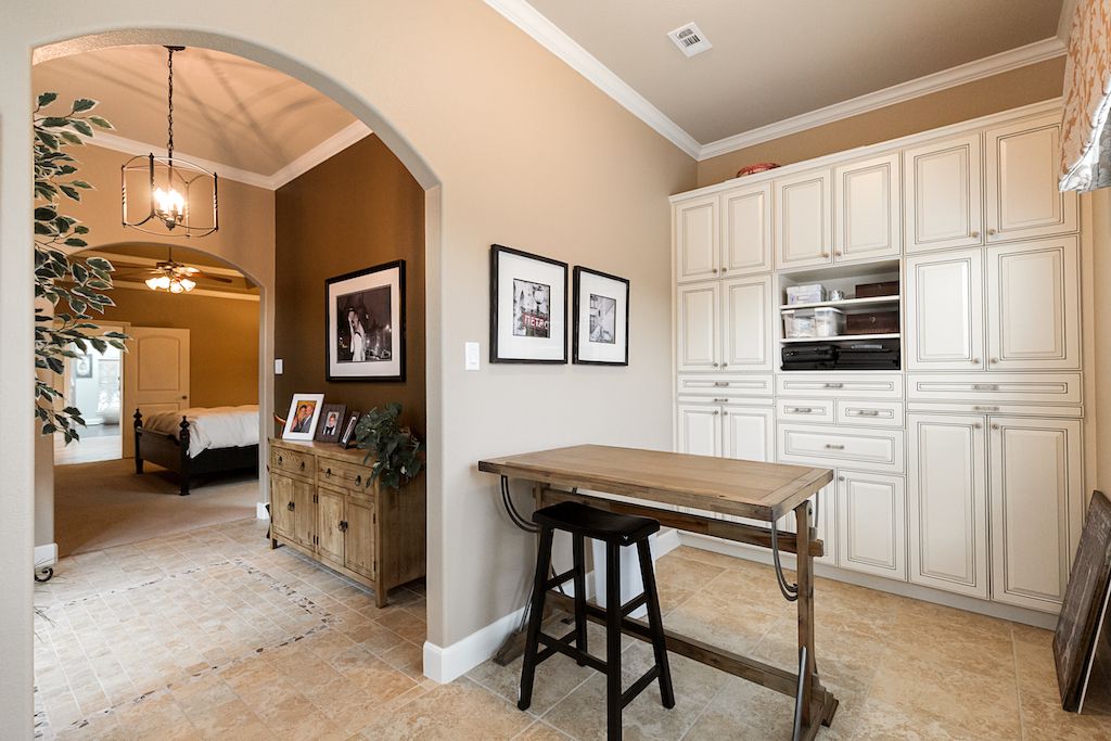 Elegant home interior with cream cabinetry, arched doorway, wooden desk, and tile flooring leading to a cozy bedroom.